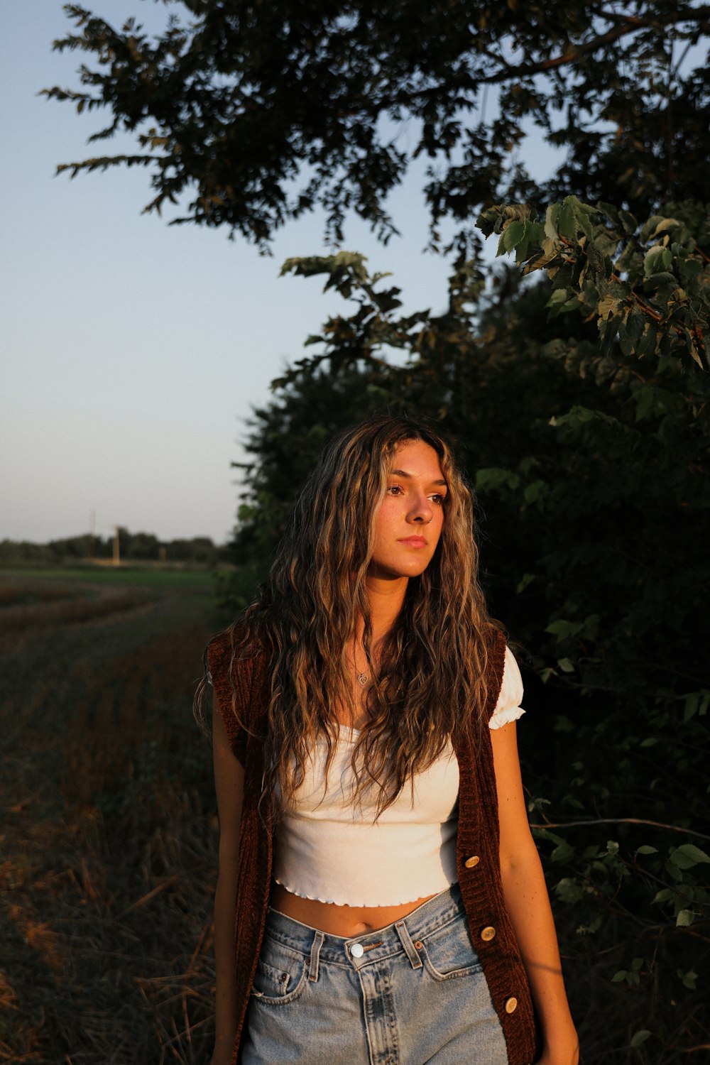 woman in white tank top standing near green tree during daytime