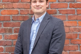 man in gray suit jacket standing beside brown brick wall
