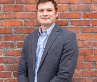 man in gray suit jacket standing beside brown brick wall