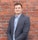 man in gray suit jacket standing beside brown brick wall