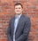 man in gray suit jacket standing beside brown brick wall