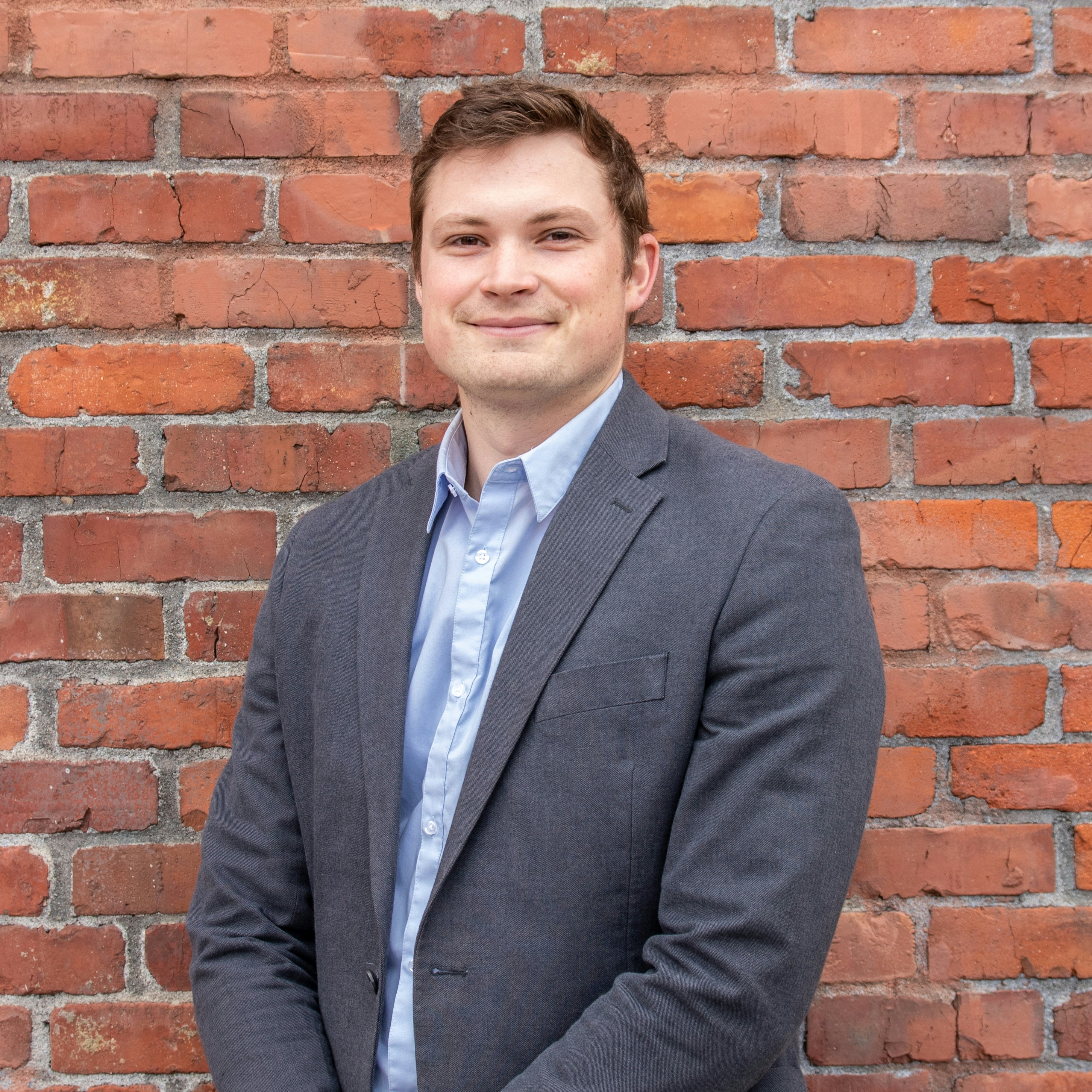 man in gray suit jacket standing beside brown brick wall