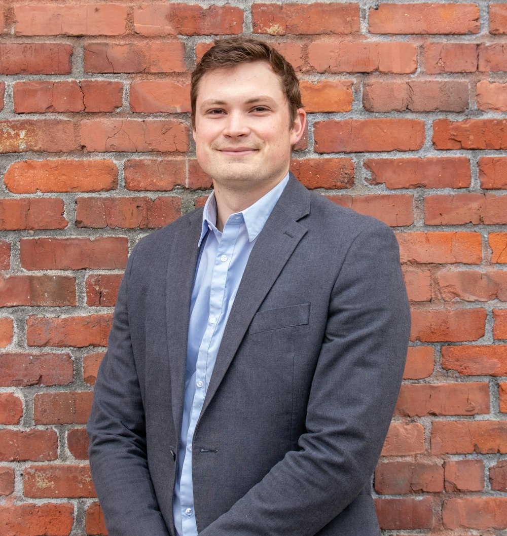 man in gray suit jacket standing beside brown brick wall