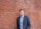 man in black suit jacket standing beside brown brick wall
