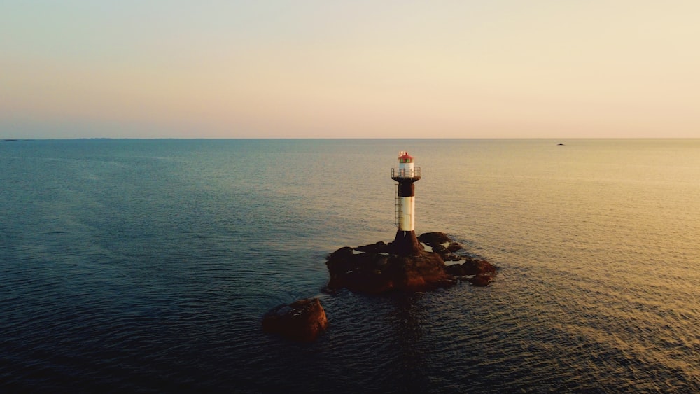 white and red lighthouse on rock formation near body of water during daytime