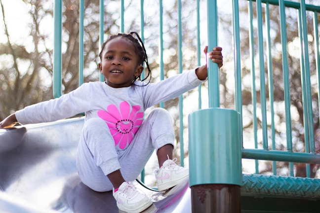 A little girl and boy playing together on a playground slide, their faces lit with pure joy.
