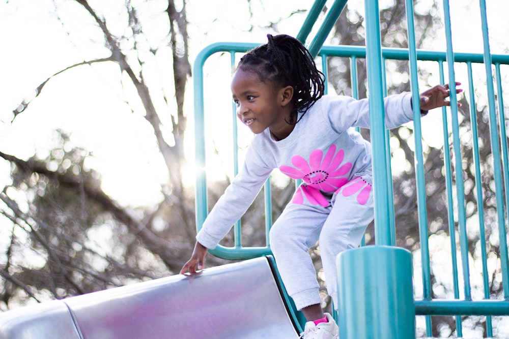 girl in pink long sleeve shirt and pink pants climbing on blue metal ladder during daytime