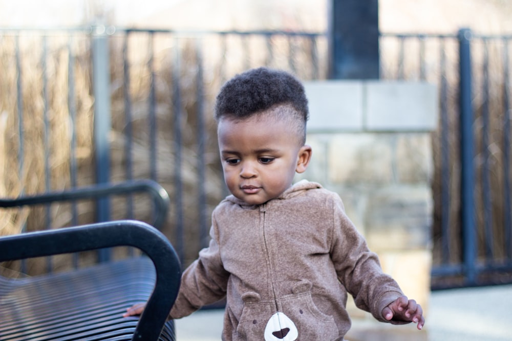 boy in brown button up jacket sitting on black metal bench during daytime