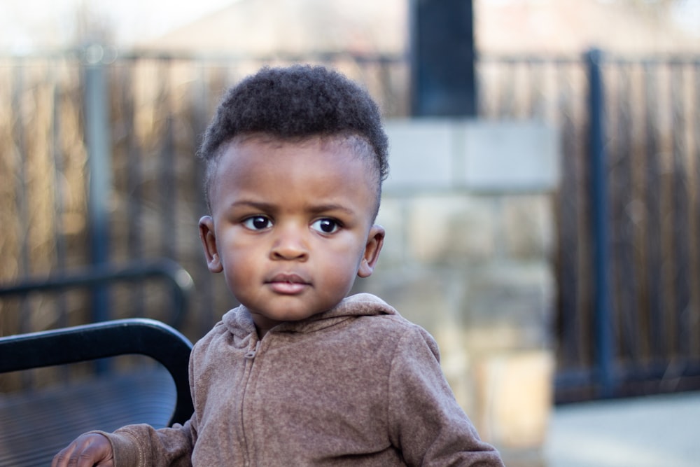 boy in brown sweater sitting on black metal bench during daytime