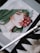A digital artwork displayed on a tablet depicts a stylized portrait of a woman with green and white hair, holding a bunch of red grapes near her lips. The image is accompanied by a digital pen resting on a textured surface, suggesting the setting is an artistic workspace.