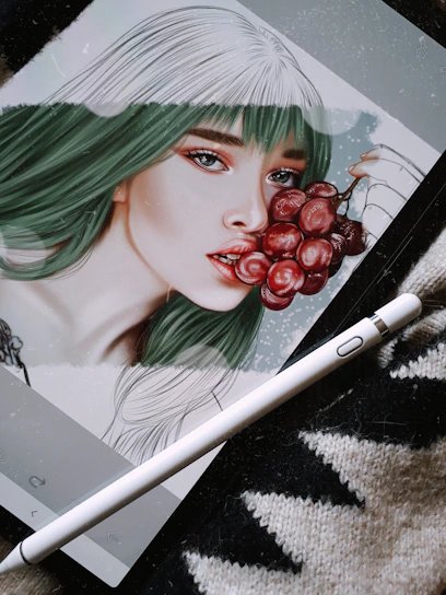 A digital artwork displayed on a tablet depicts a stylized portrait of a woman with green and white hair, holding a bunch of red grapes near her lips. The image is accompanied by a digital pen resting on a textured surface, suggesting the setting is an artistic workspace.