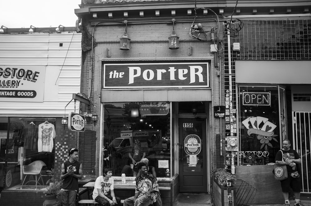 grayscale photo of man and woman sitting on bench in front of store