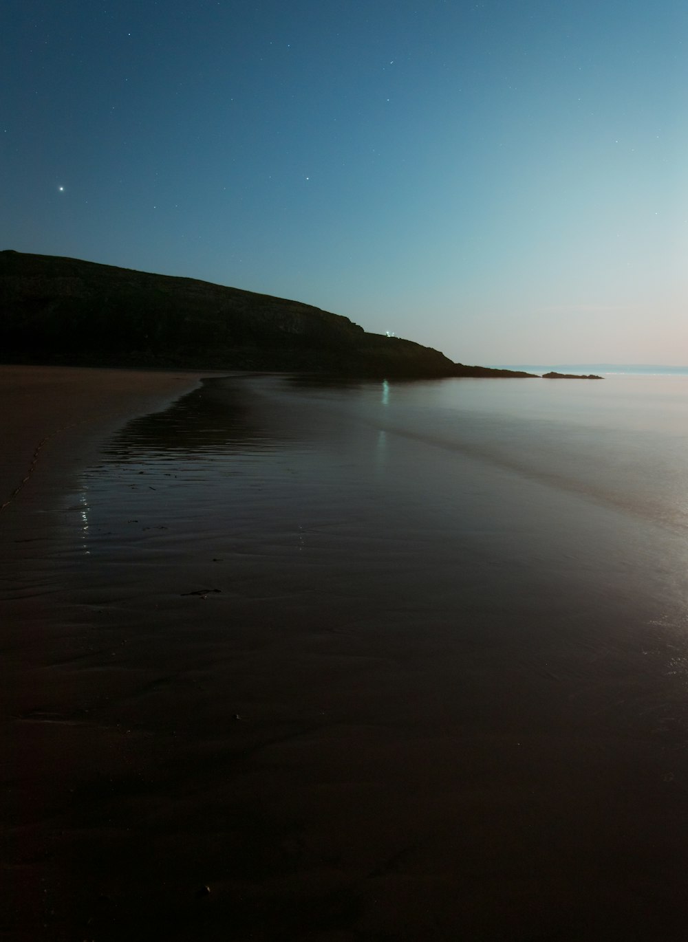 calm sea near mountain under blue sky during daytime