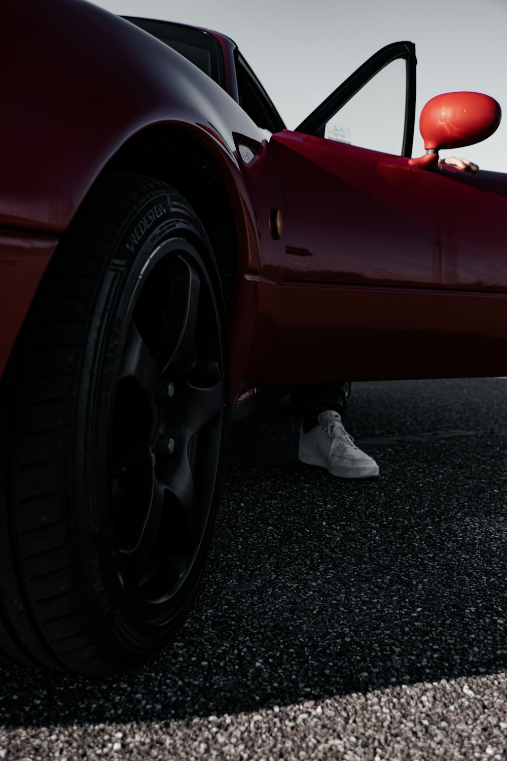 person in white pants and white shoes standing beside red car