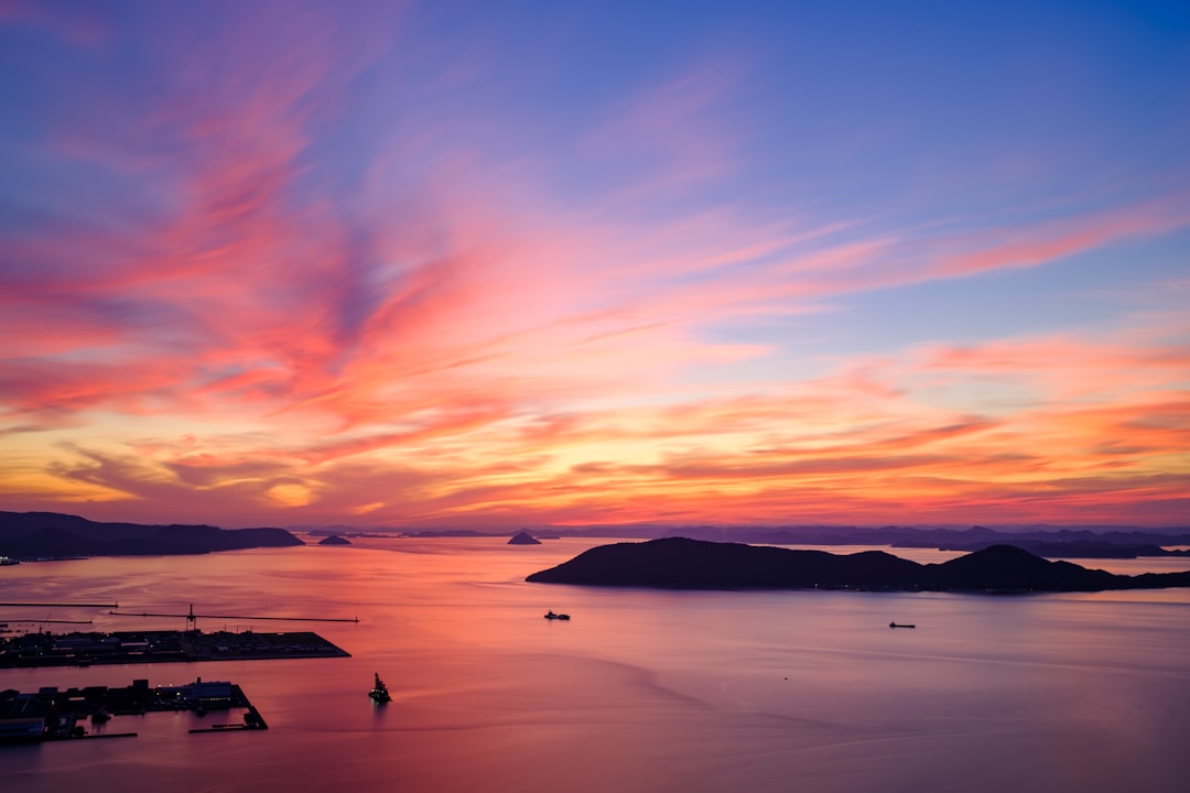 silhouette of mountain beside body of water during sunset