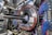 A complex industrial setup with a large circular machine at the center, surrounded by numerous cables of various colors, primarily blue and black. The machinery is metallic with a shiny texture and intricate panels. The environment appears highly technical, resembling a laboratory or a facility handling high-tech equipment.