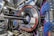 A complex industrial setup with a large circular machine at the center, surrounded by numerous cables of various colors, primarily blue and black. The machinery is metallic with a shiny texture and intricate panels. The environment appears highly technical, resembling a laboratory or a facility handling high-tech equipment.