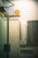 A tiled wall featuring a directory sign listing various business names and room numbers in a building. There is a security camera sign with an orange logo attached above. The setting appears to be an indoor corridor or lobby area with a glass door on the left side.