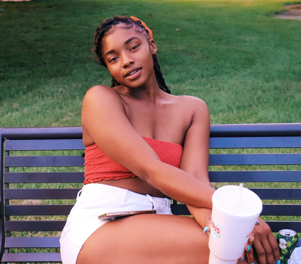 woman in red tank top sitting on blue bench holding white disposable cup