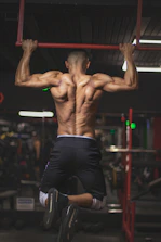 Athlete mid pull-up with red glow highlighting muscle definition.