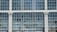 A section of a large window comprising multiple glass panes arranged in a grid pattern. Some of the panes are broken or missing. The window is framed by white pillars featuring ornate decorative designs at the top.