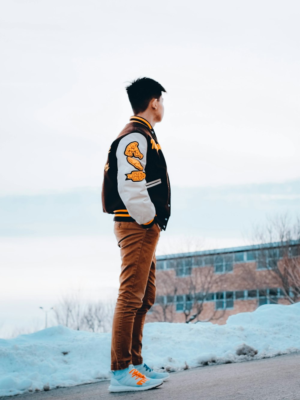 uomo in camicia a maniche lunghe in bianco e nero e pantaloni marroni in piedi su terreno coperto di neve