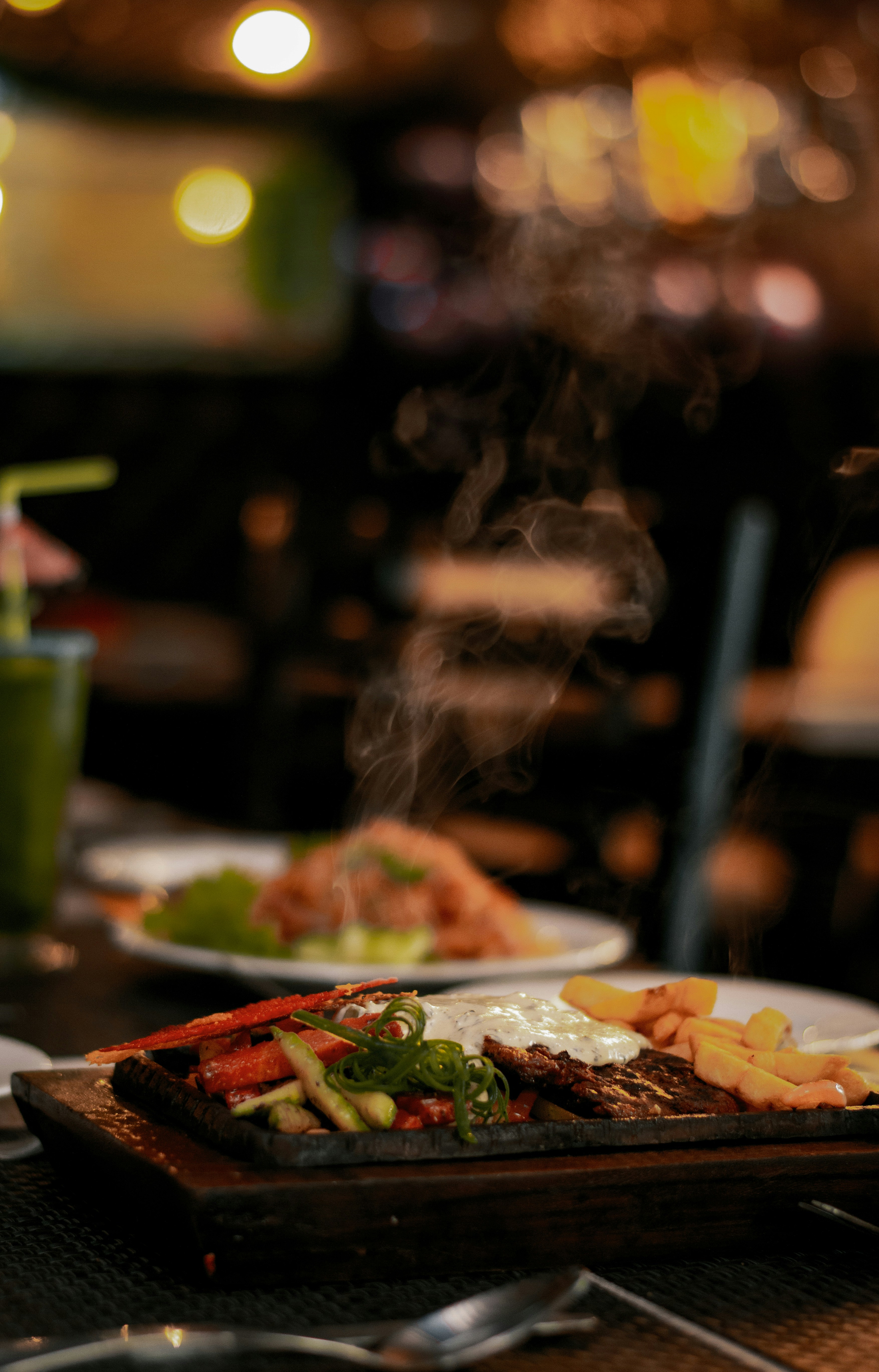 Sizzling mixed grill spread for a large group on a long table, warm amber restaurant lighting, dark moody atmosphere