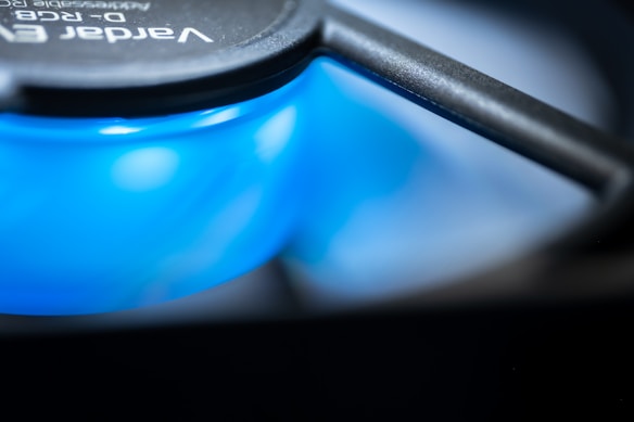 A close-up view of a computer cooling fan, focusing on the blue spinning blades under the black frame. The image captures the dynamic motion and the glossy texture of the fan blades, with text visible on the fan indicating brand details but not fully readable.