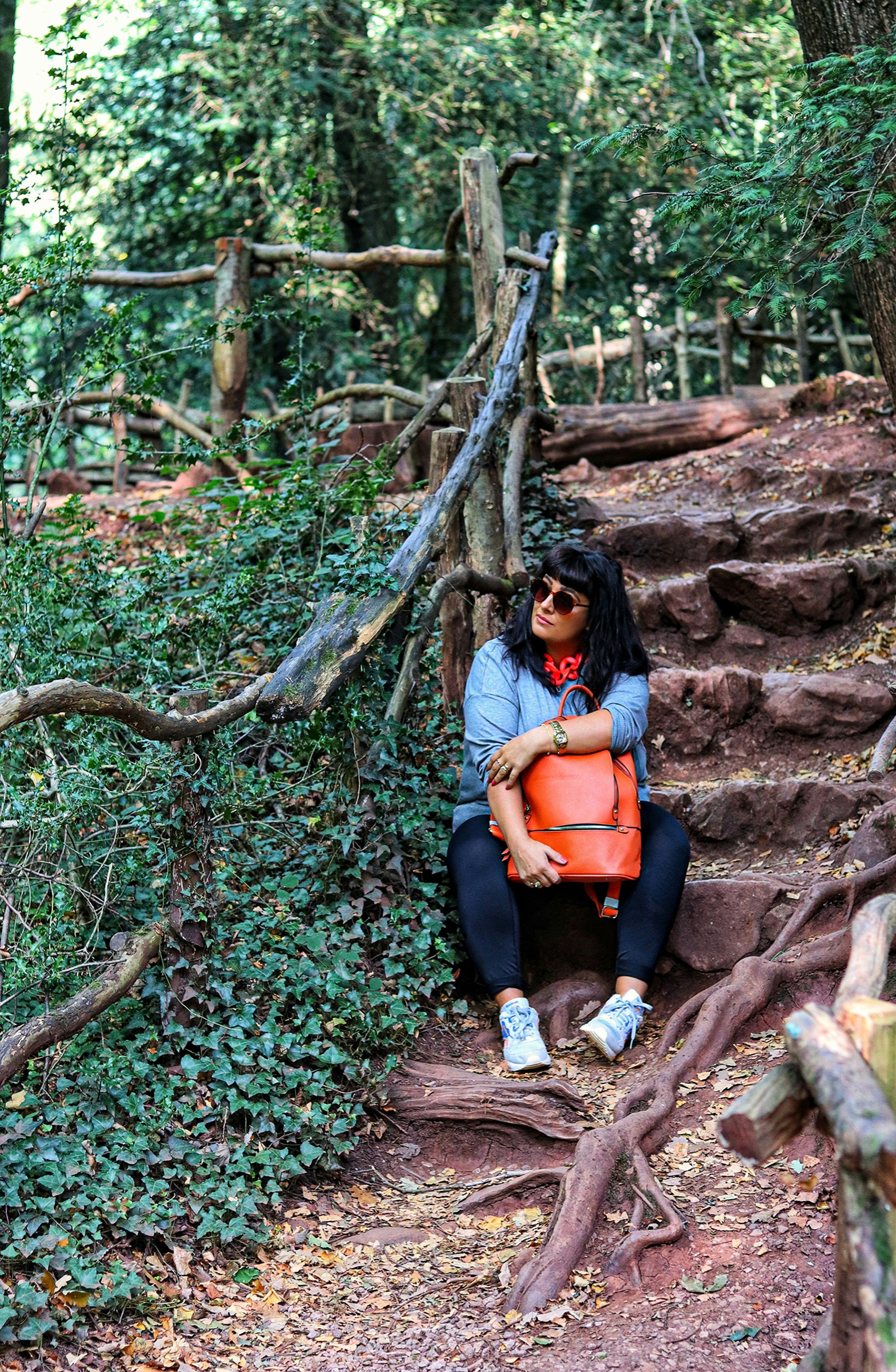Frau in orangefarbenem Hemd und schwarzer Hose sitzt auf braunem Felsen