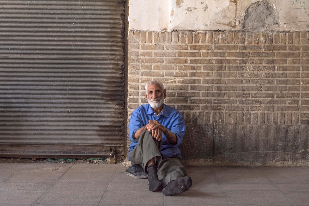 man in blue jacket sitting beside brown brick wall