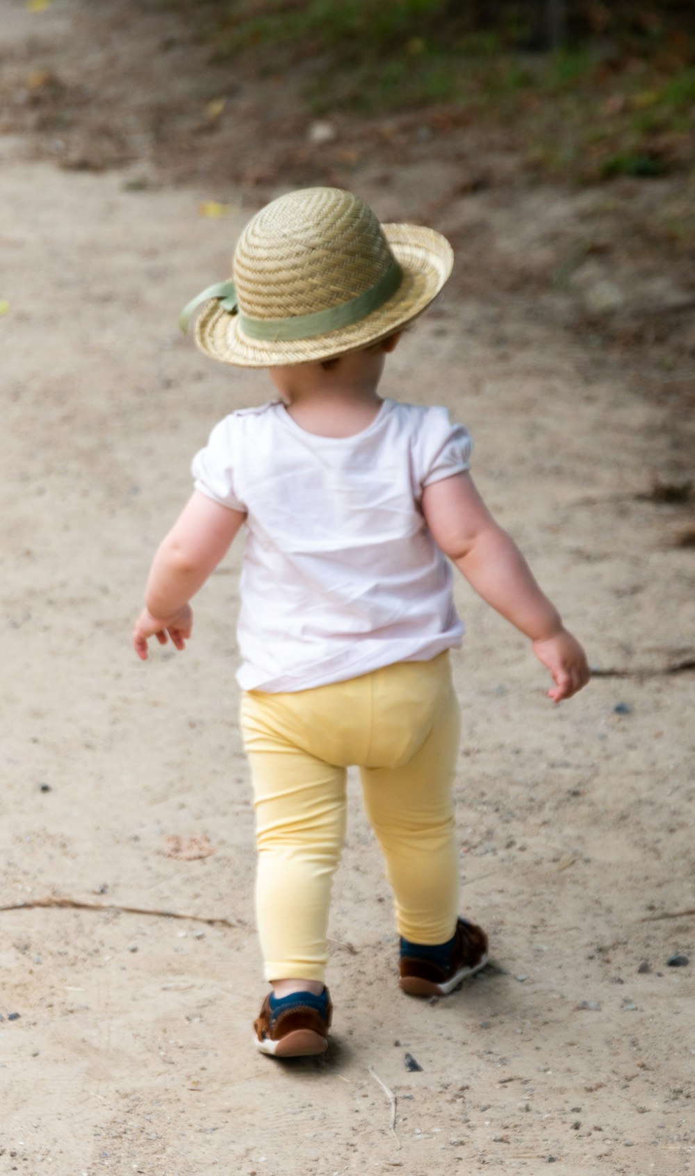 白いシャツと黄色い短パンを着た子供が昼間、砂の上を歩いている