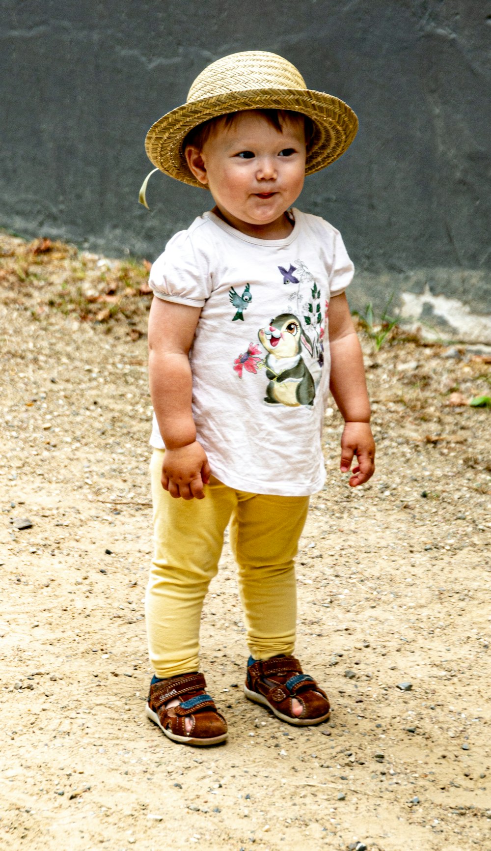child in white crew neck t-shirt and yellow pants standing on brown sand during daytime