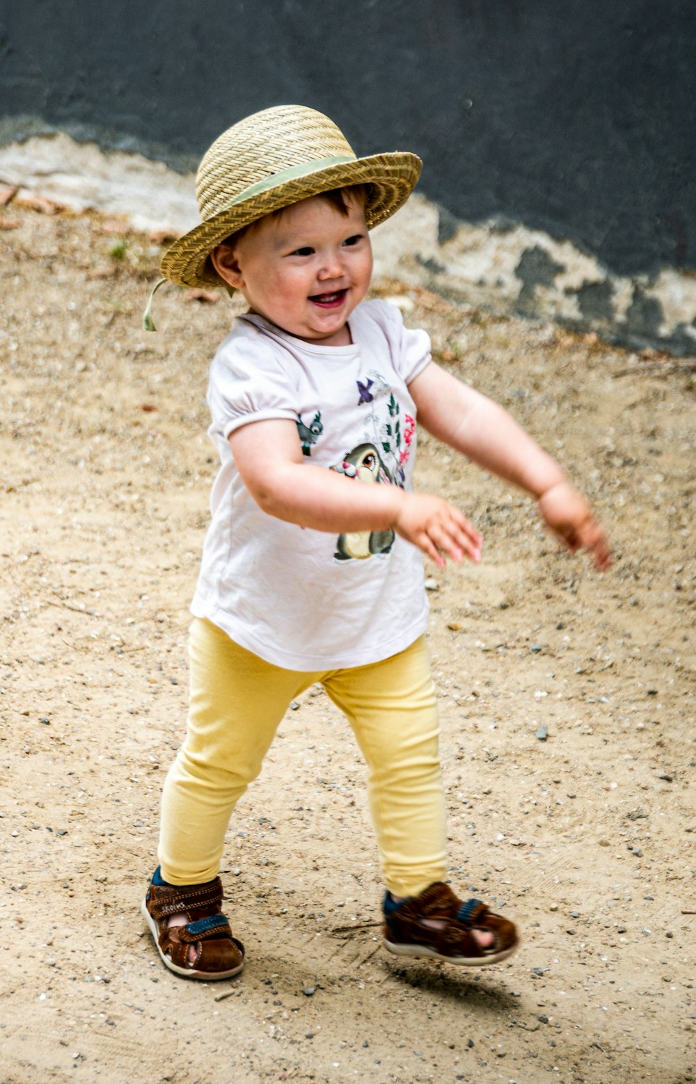 girl in white shirt and yellow pants wearing brown straw hat