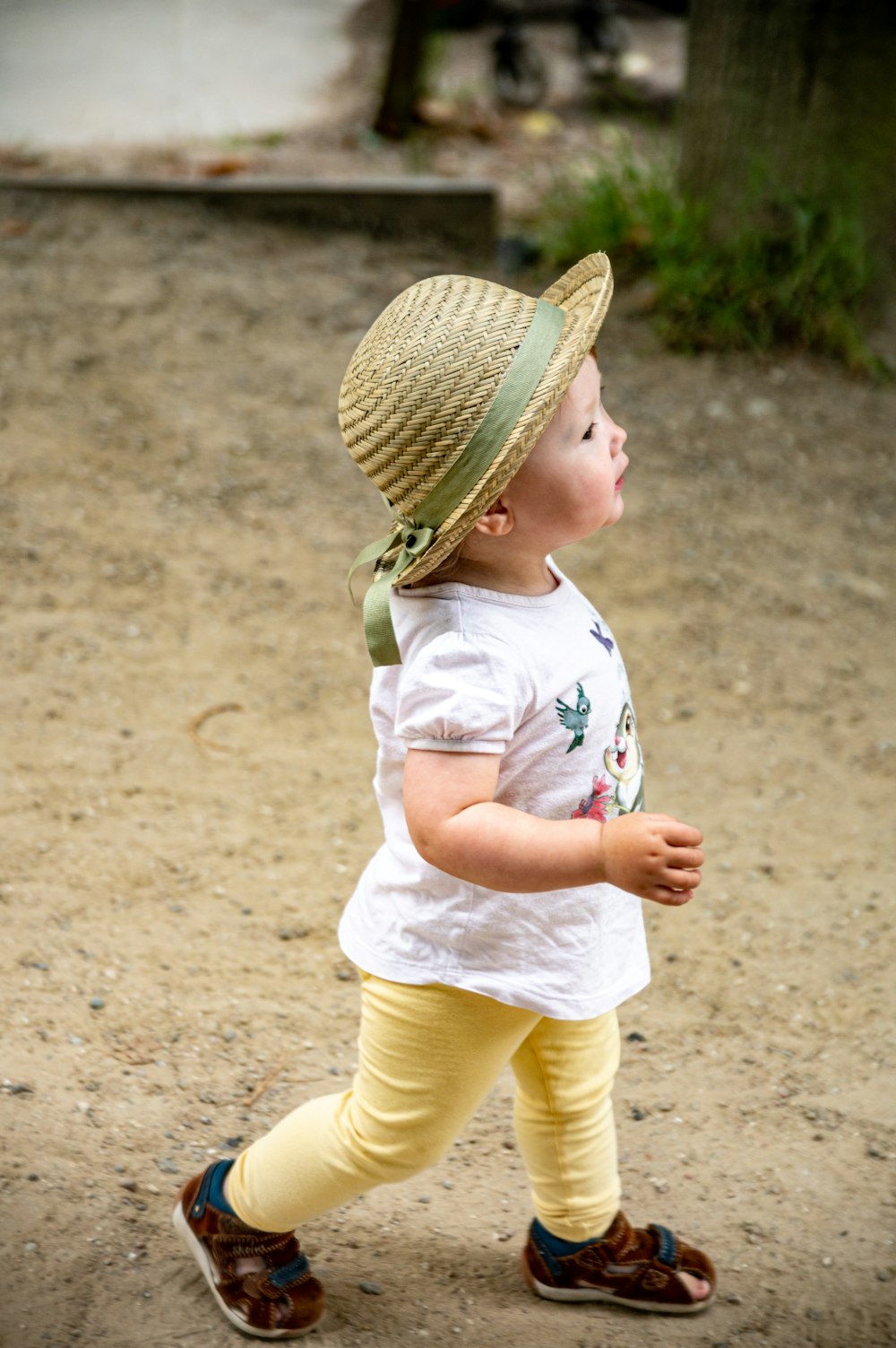 girl in white t-shirt and yellow pants wearing brown woven hat