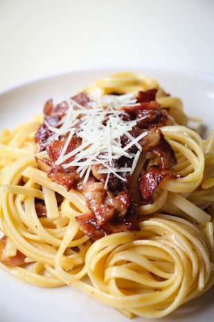 Close-up of a steaming bowl of pasta with rich carbonara sauce and crispy pancetta.
