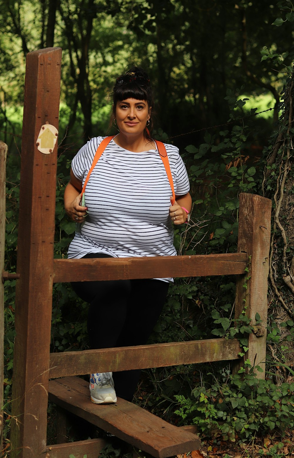 Mujer con camisa a rayas blancas y negras y pantalones negros de pie sobre un puente de madera marrón