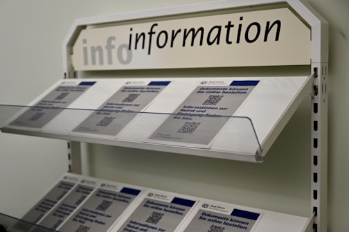 A display rack filled with informational brochures is seen. The brochures have a blue and white color scheme and feature text with QR codes. Above the rack, a sign reads 'info information' in uppercase and lowercase letters.