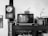 A retro setting featuring an old television displaying Chinese characters and the phrase 'BOOK RESCUES YOU'. A small pumpkin is placed on top of the TV. To the left, a vintage wooden wall clock shows the time. A floral decoration and some figurines are positioned next to the TV on a wooden cabinet. Books and a decorative flower in a pot are also visible.