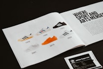 A magazine spread featuring a timeline of sneakers from 1970 to 2020. The left page displays images of six different sneakers, each labeled with a year: 1970, 1985, 1993, 2001, 2015, and 2020. The right page includes bold text stating 'WHERE SPORT AND ARTS MERGE' along with a paragraph of text underneath. The sneakers are of varying colors, with notable ones being blue-striped, black, and orange.
