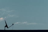 A silhouette of a satellite dish with a cable is positioned on a flat surface against a clear blue sky. A few faint clouds are visible, creating a serene and minimalistic scene.