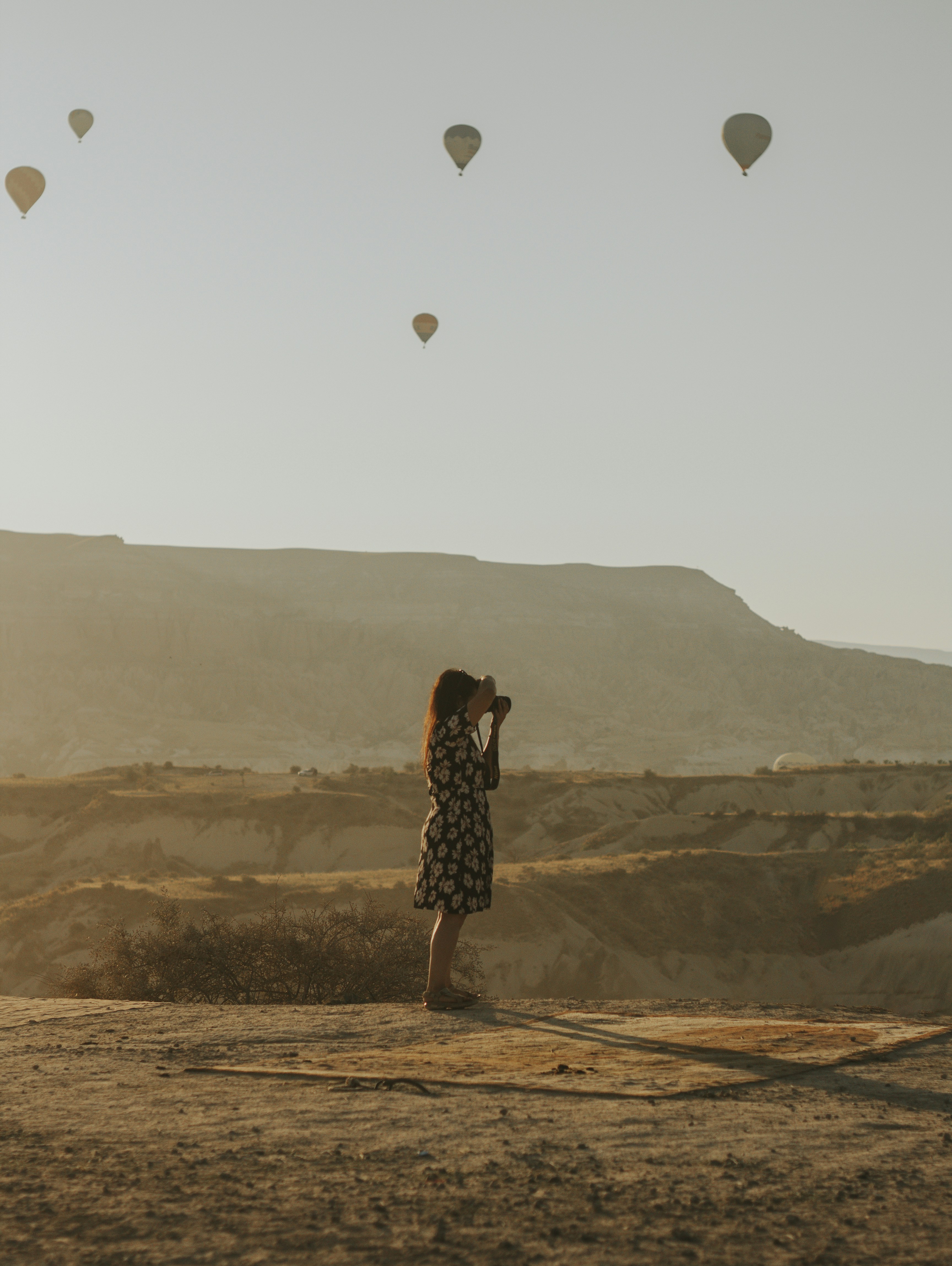 woman in black and white polka dot dress standing on brown field with hot air balloons