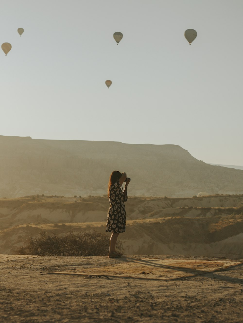 woman in black and white polka dot dress standing on brown field with hot air balloons