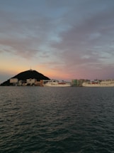 A calm harbor scene with cargo ships docked under a clear sky at sunset.