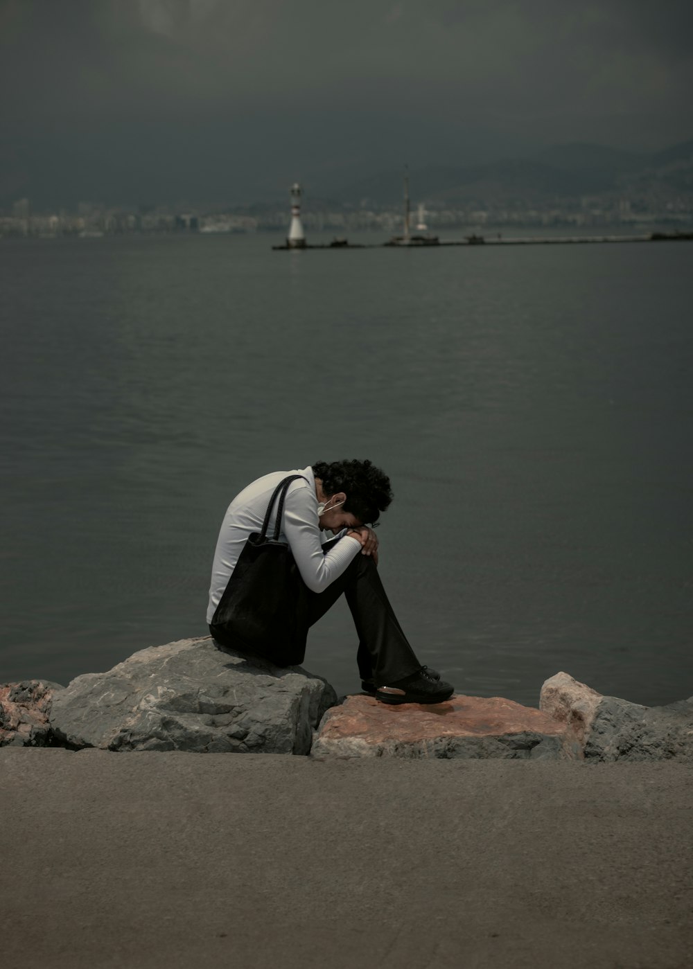 man in black and white jacket sitting on brown rock near body of water during daytime