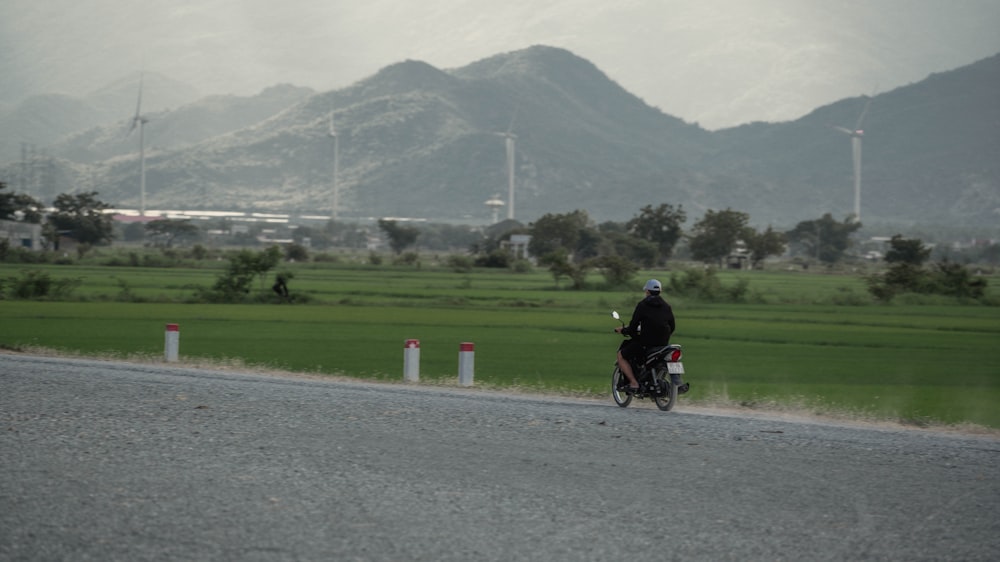 uomo in camicia nera che guida la motocicletta sulla strada asfaltata grigia durante il giorno