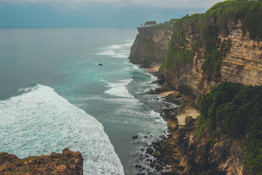 brown and green cliff beside body of water during daytime