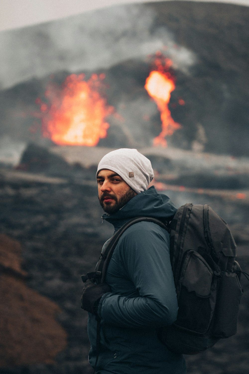 man in black jacket and white knit cap standing on brown rock