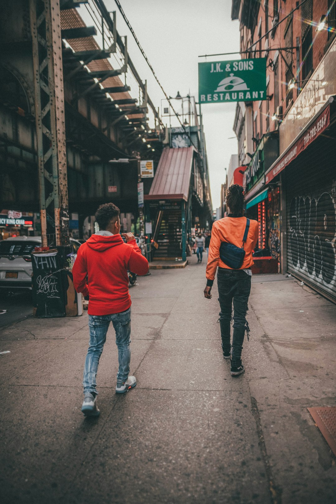 man in red hoodie and blue denim jeans walking on sidewalk during daytime