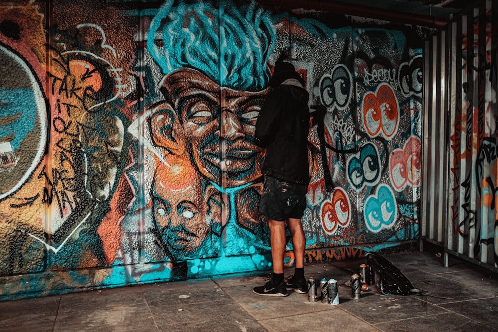 man in black jacket standing beside graffiti wall