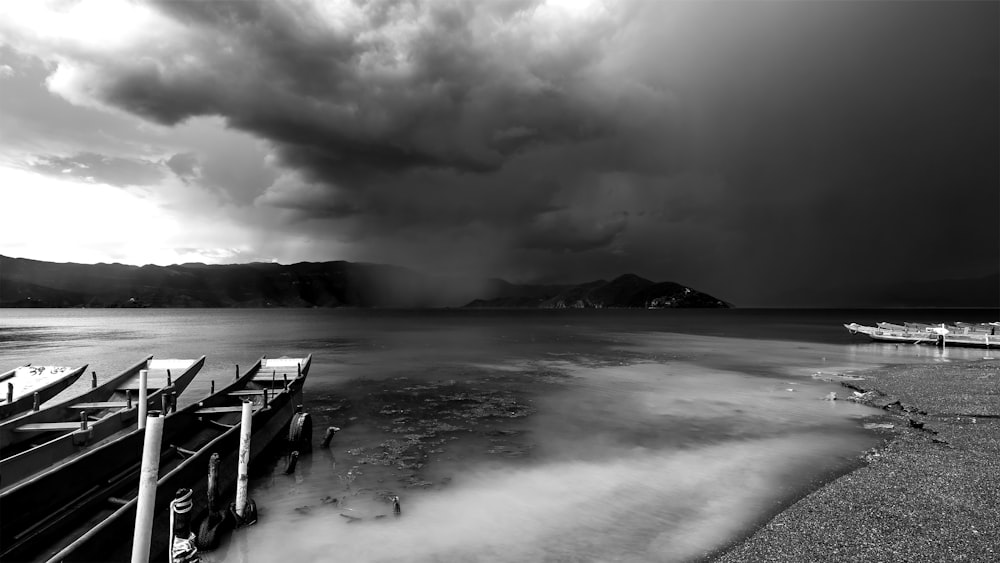 grayscale photo of beach with bench on the shore